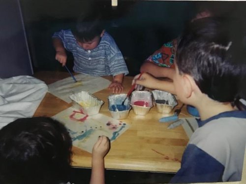 4 homeschool children sitting around a table and painting pictures.