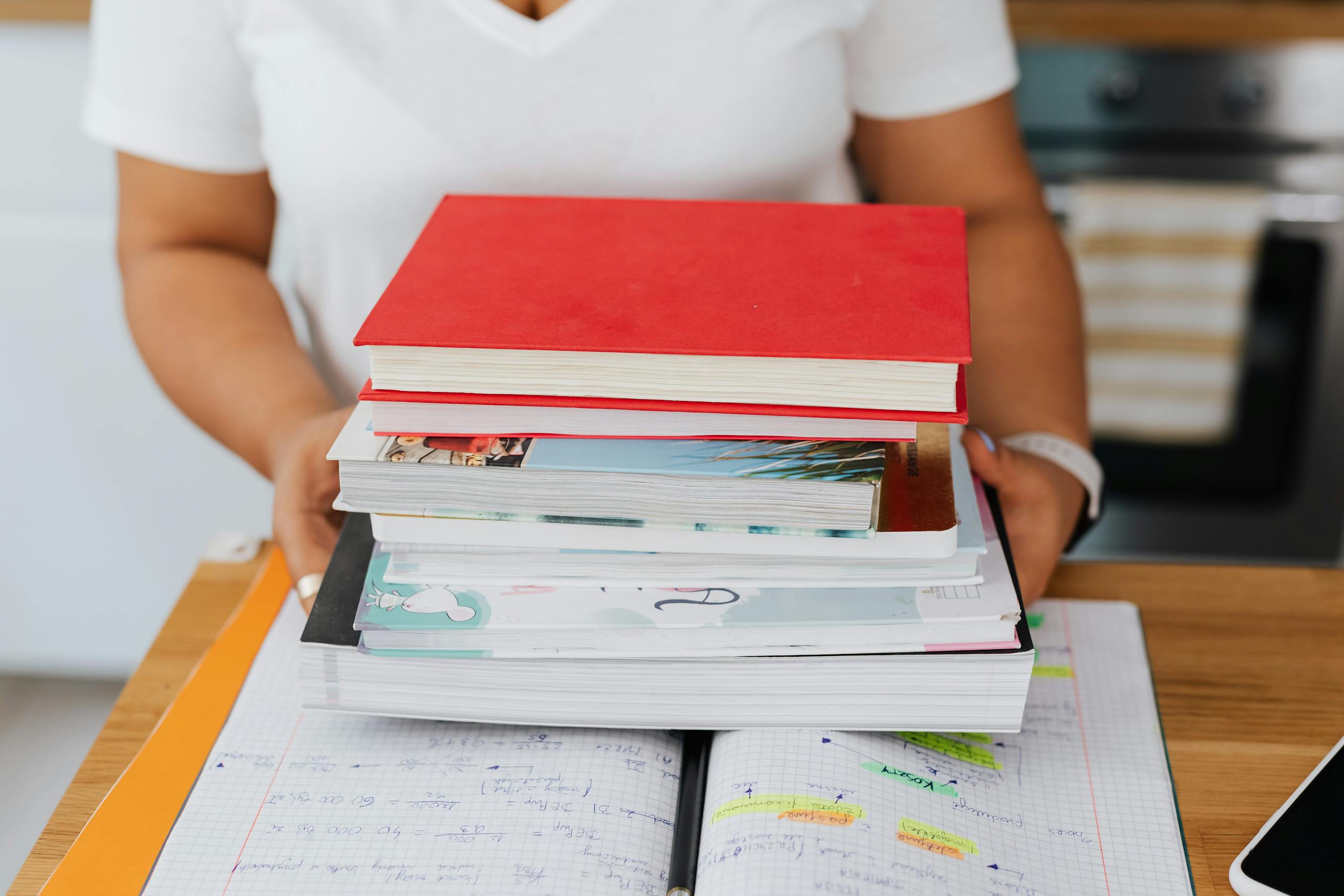 Close-up of a person holding a stack of colorful homeschool books over an open notebook.