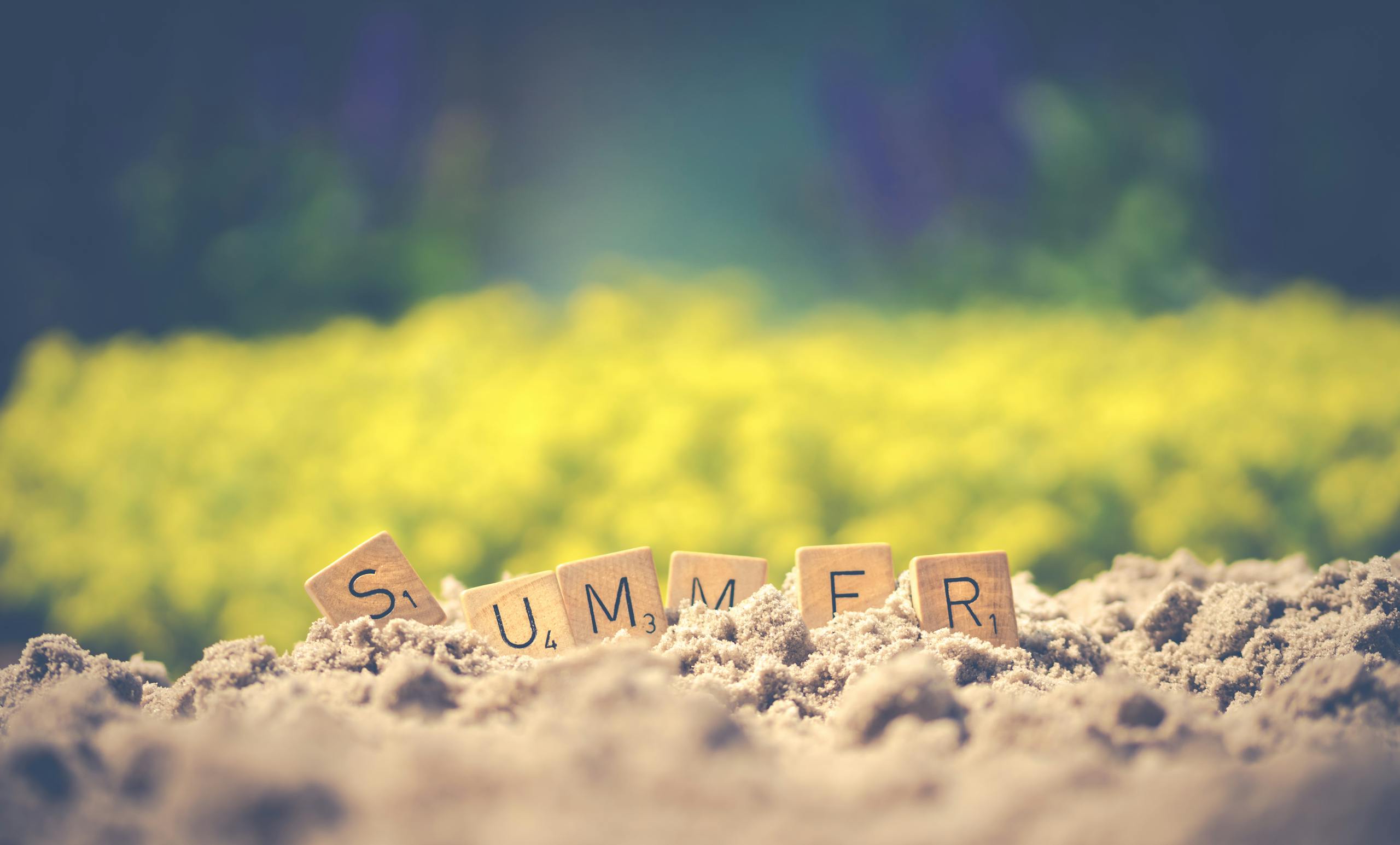 Scrabble tiles forming the word 'summer' in sand with a blurred background, evoking warm vibes. For blog post Homeschool and summer School