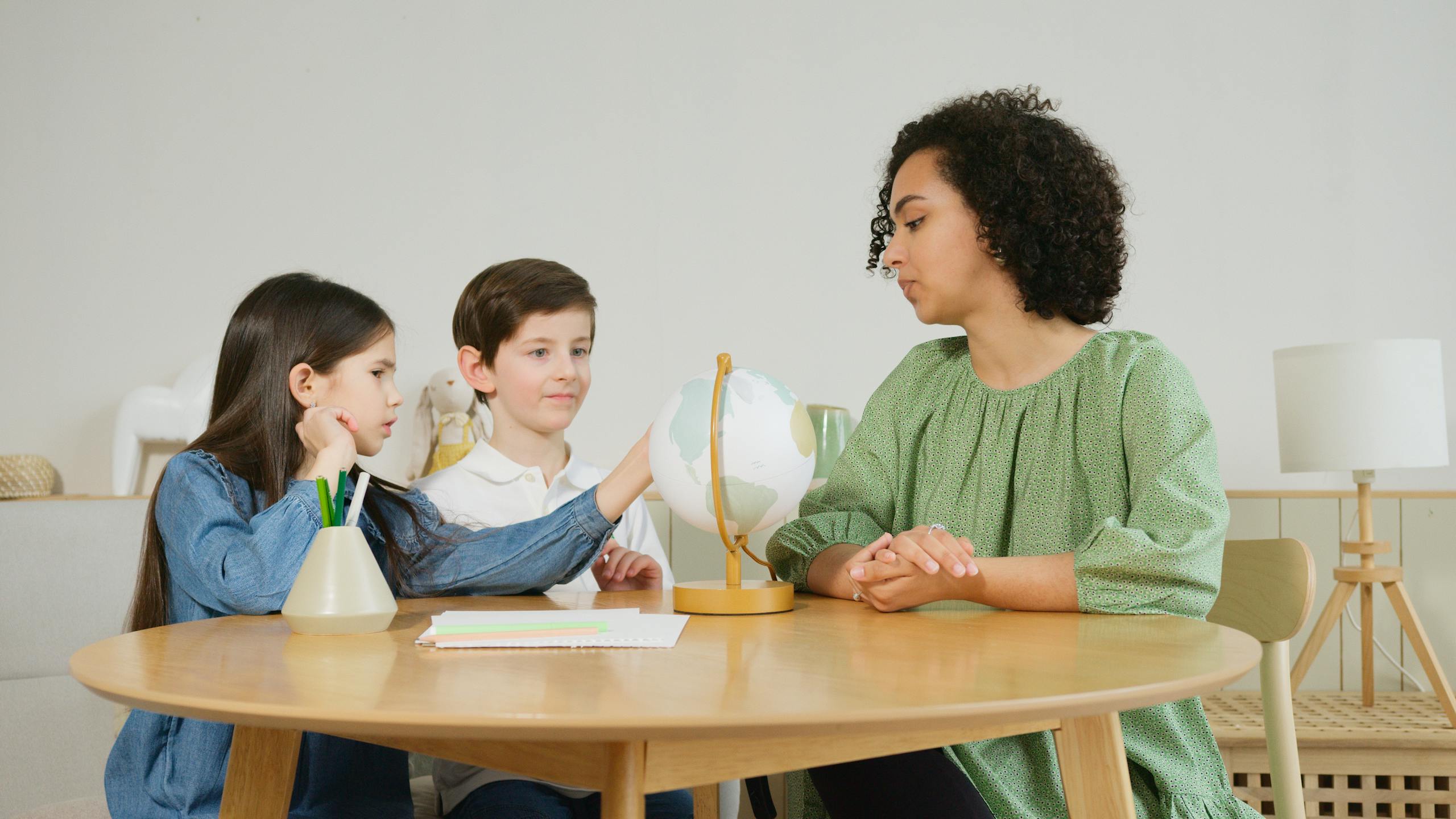 A homeschool mom guides two children in a geography lesson using a globe.