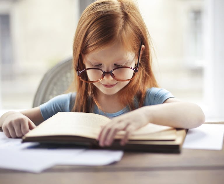 A young homeschooled girl with glasses intently reads a book indoors, embodying the essence of learning and discovery. Homeschooling a Child with Dyslexia