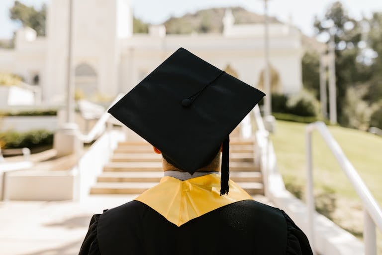 Back view of a homeschool graduate in a cap and gown standing outdoors facing a building. Is Homeschooling Enough?
