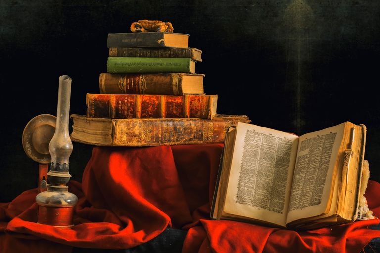 An artistic still life featuring a stack of vintage books and an olive lamp on rich red cloth. Mystery of history curriculum review.